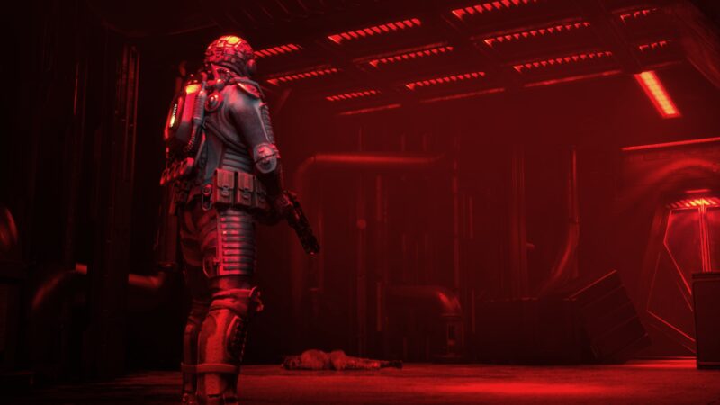 Colton in armour in a corridor flooded with red alarm light, a body on the floor behind him