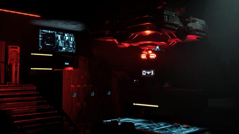 Overhead machinery under red light, monitors still running on the far wall